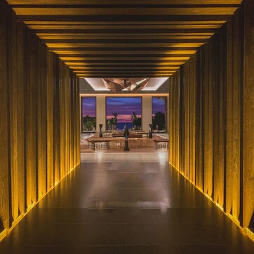 A corridor with wooden paneling and a view of a sunset through large windows.