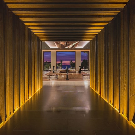 A corridor with wooden paneling and a view of a sunset through large windows.