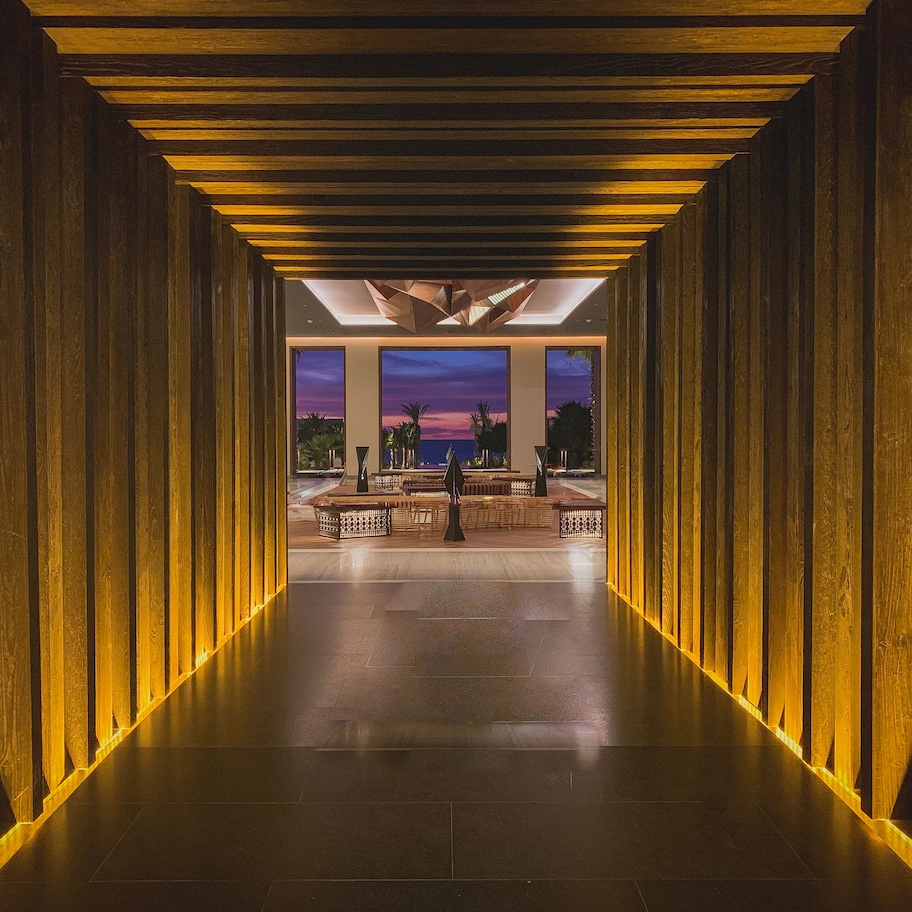 A corridor with wooden paneling and a view of a sunset through large windows.