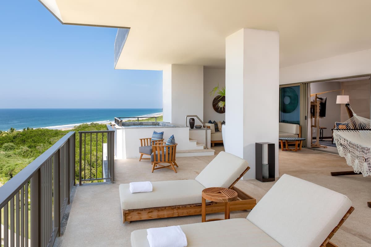 A balcony with a view of the ocean, a seating area with a table and chairs, and a hammock.