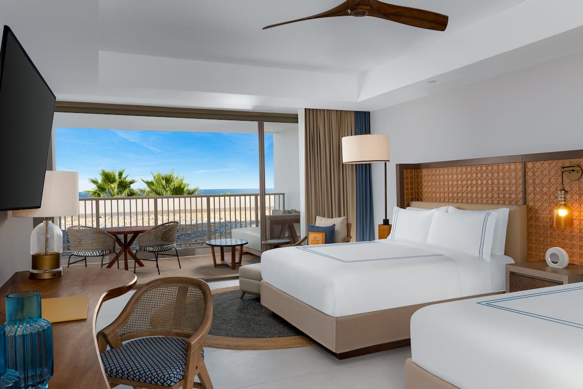 A hotel room with a large bed, a desk with a lamp, a chair, and a view of the beach.
