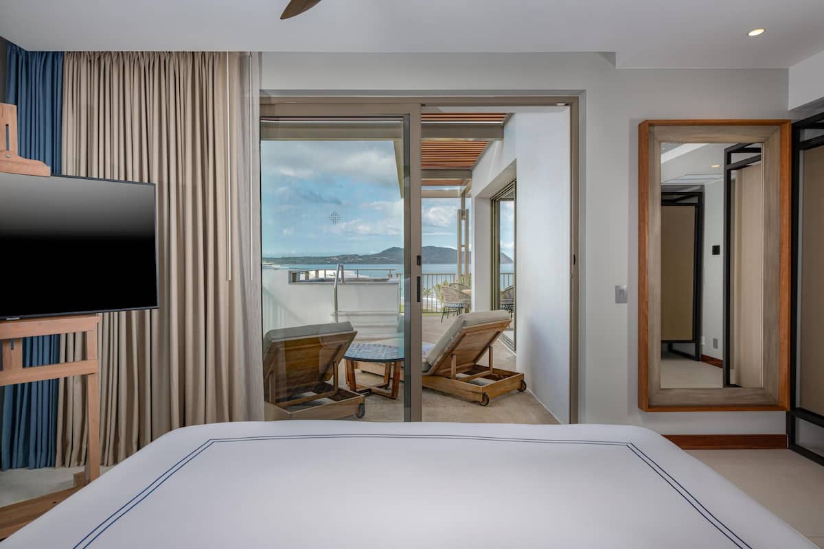 A hotel room with a bed, a TV, a balcony with a table and chairs, and a view of the sea.
