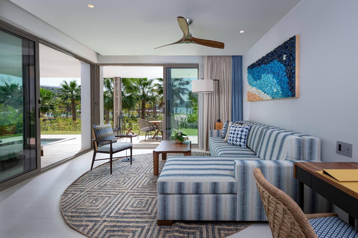 A modern living room with a large window, a ceiling fan, a striped sofa, a round rug, and a dining area.
