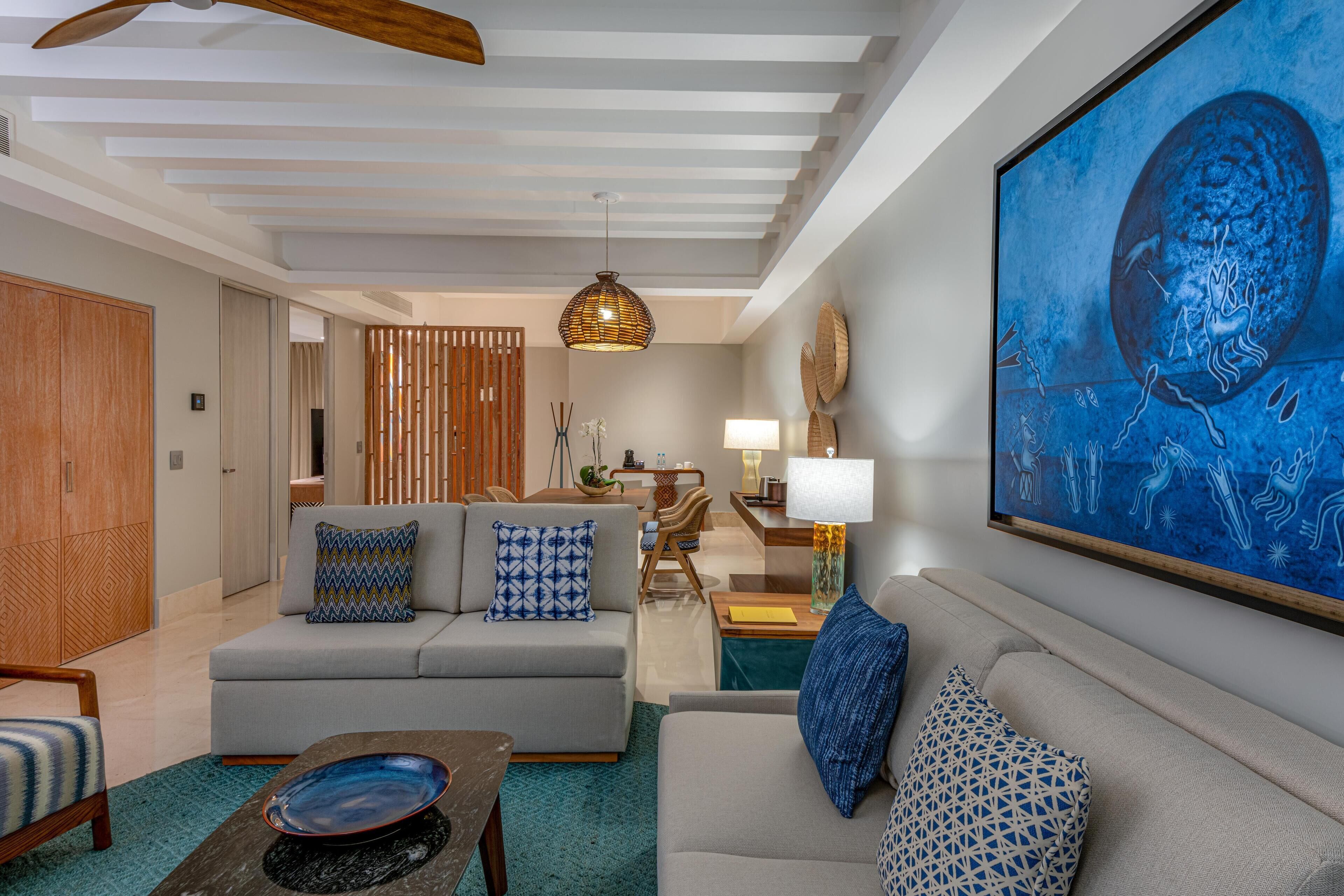 Un salon moderne avec un canapé gris, des coussins à motifs bleus, une table basse en bois et un grand tableau abstrait accroché au mur.