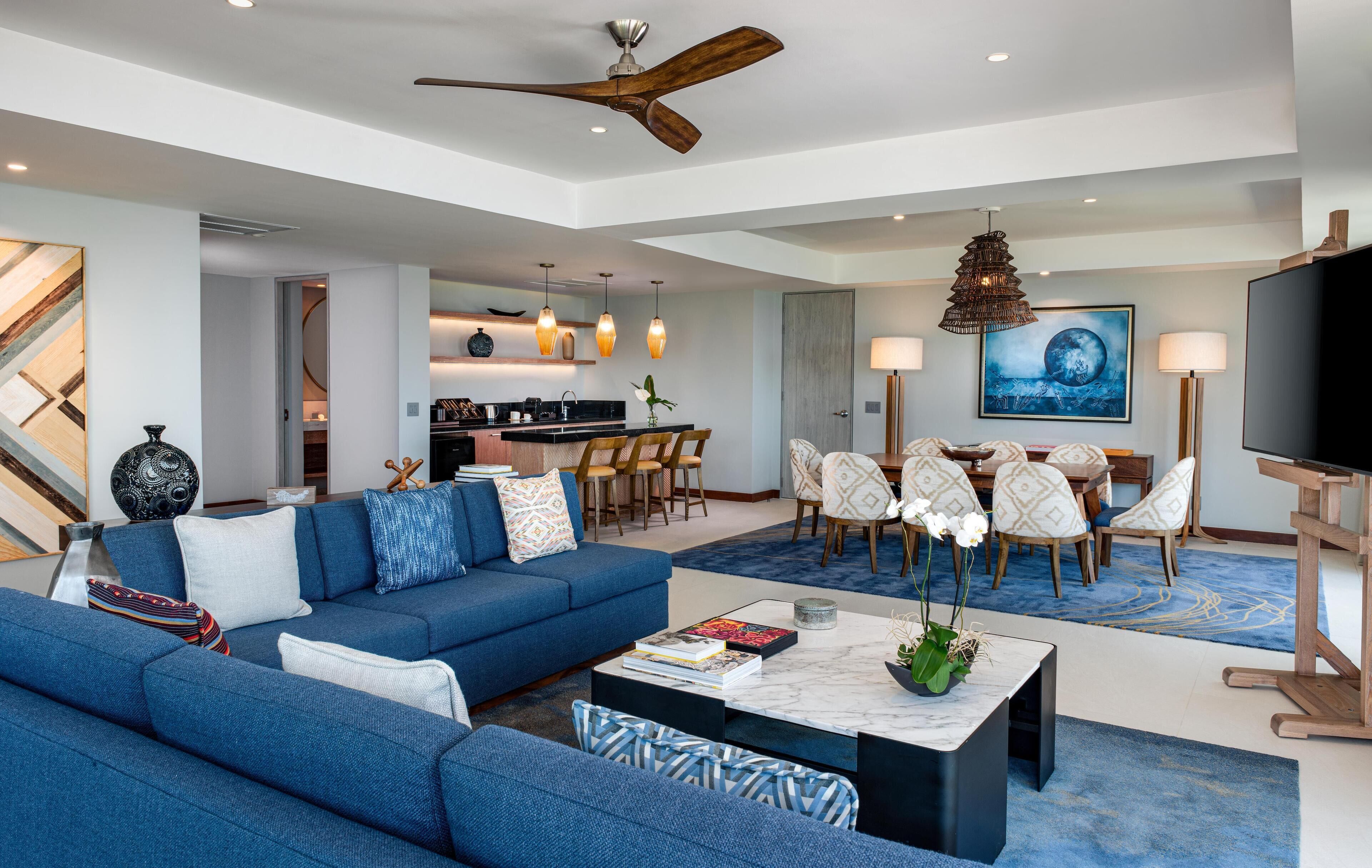 A modern living room with a blue sofa, a coffee table, and a dining area with chairs and a table.