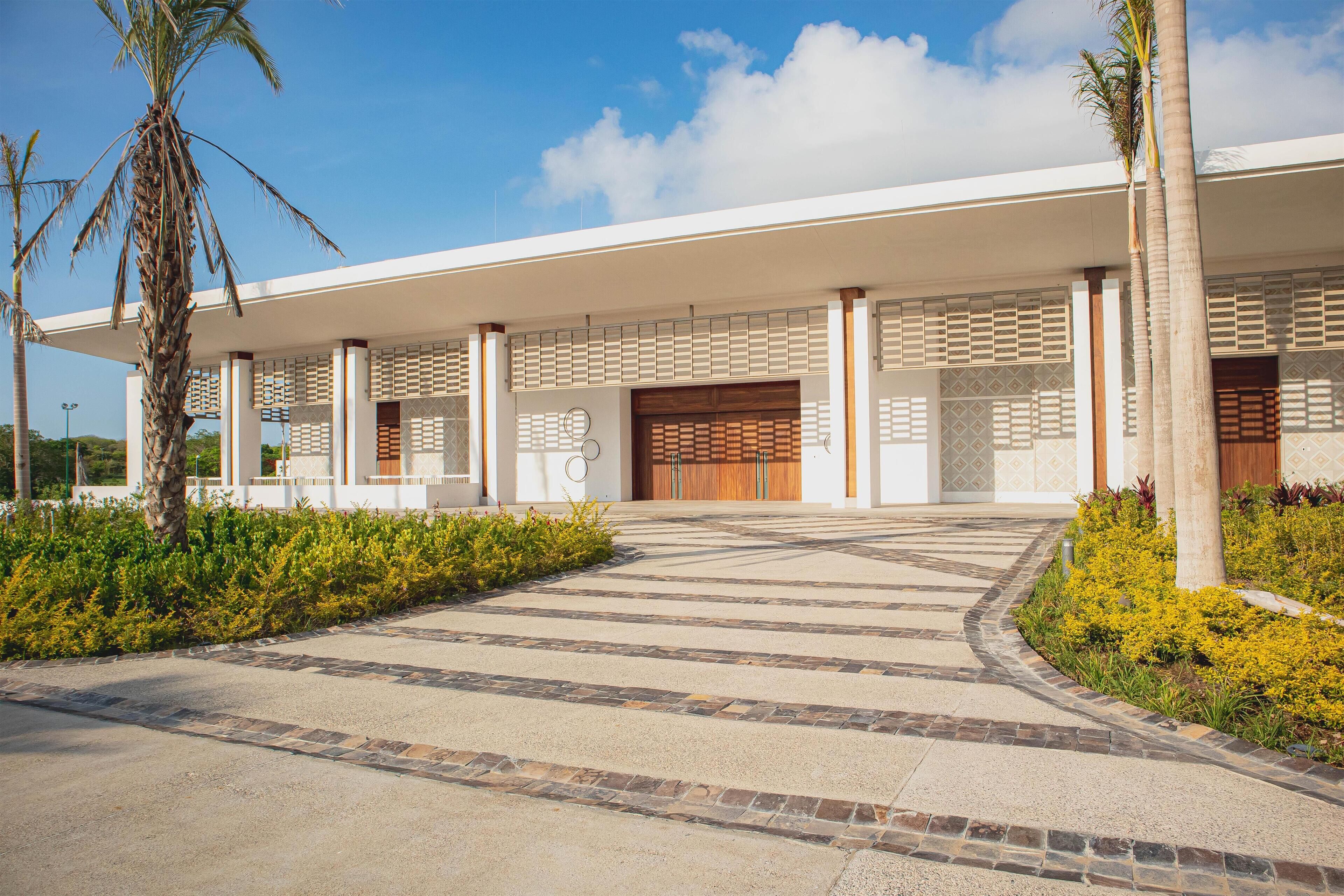 A modern building with a covered entrance, palm trees, and a paved pathway.