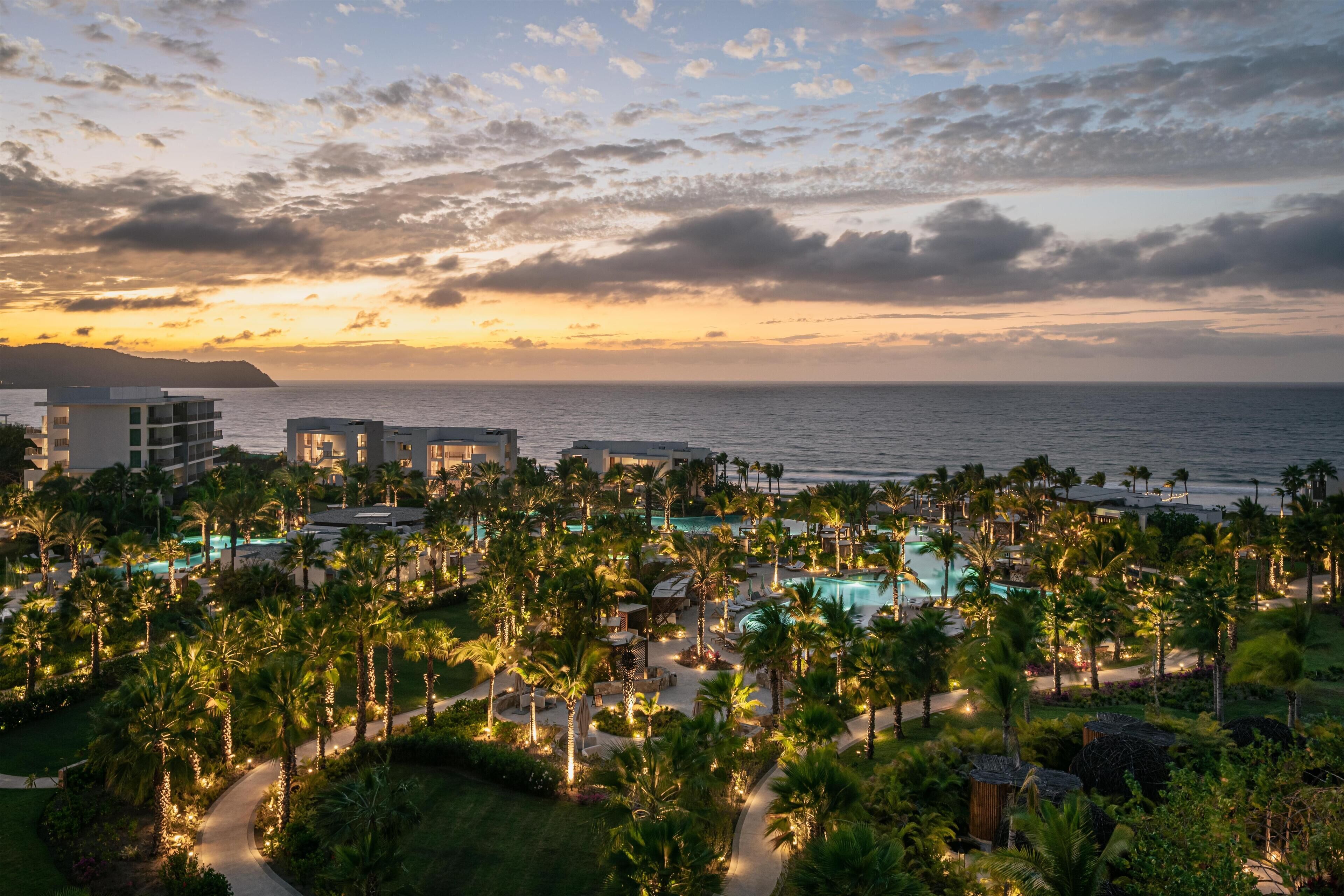 A resort with a pool area surrounded by palm trees, overlooking the ocean.