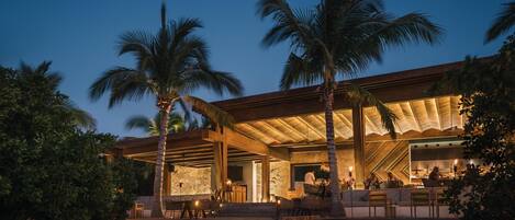 A modern resort with a covered outdoor area, palm trees, and a bar/lounge area.