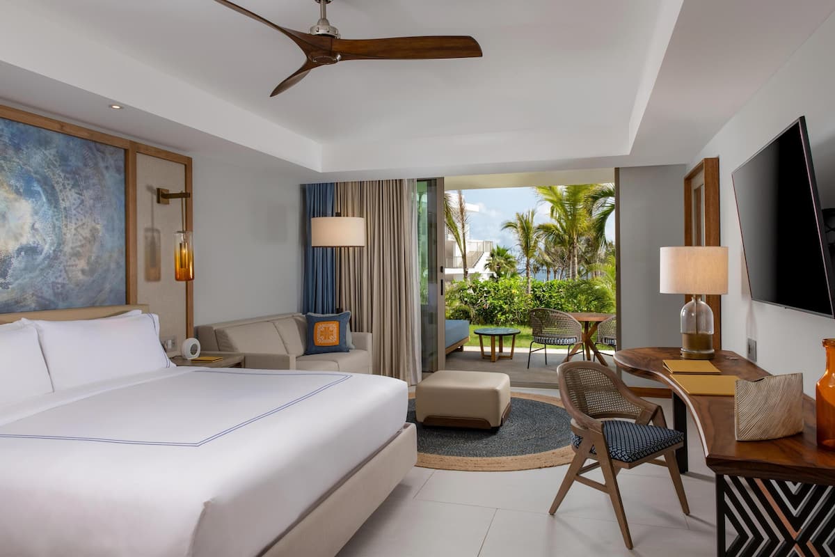 A hotel room with a large bed, a desk with a TV, a chair, and a view of the outdoors.
