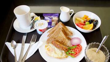 A tray with breakfast items including toast, eggs, sausage, and a bowl of fruit.