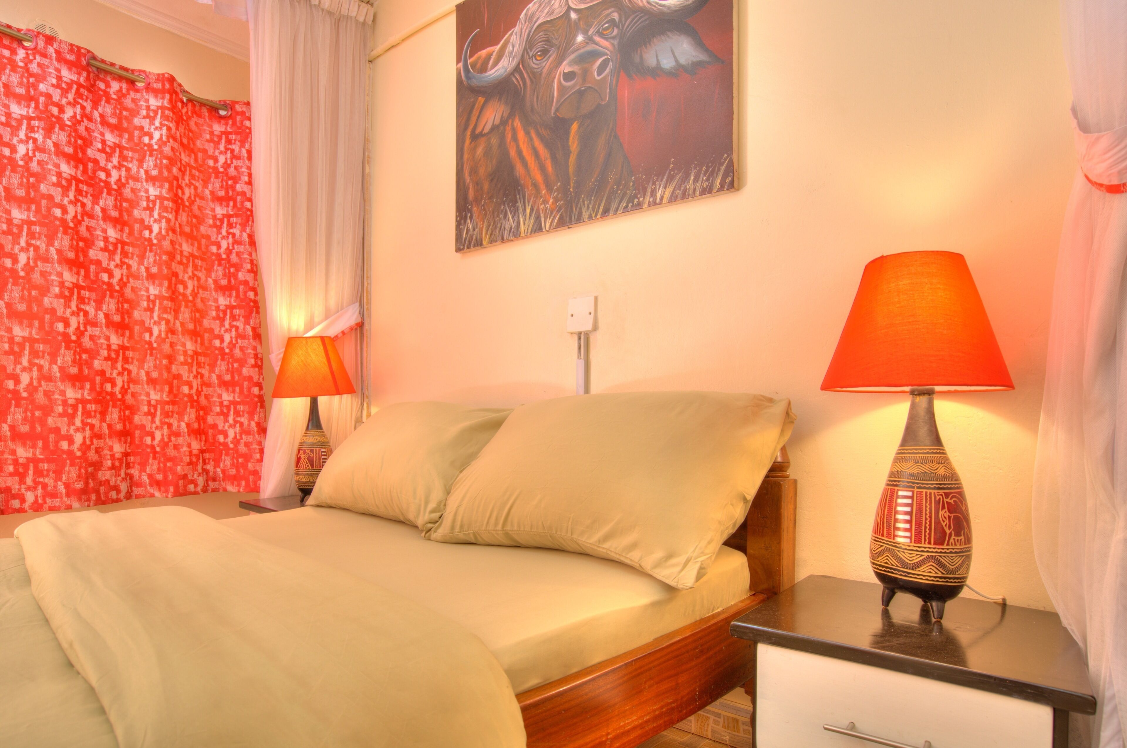 A bedroom with a bed, two bedside lamps, a wall painting, and a curtain.