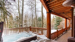 A wooden deck with a hot tub surrounded by snow, overlooking a forest. - 3390 Sun Ridge Dr (Park City)