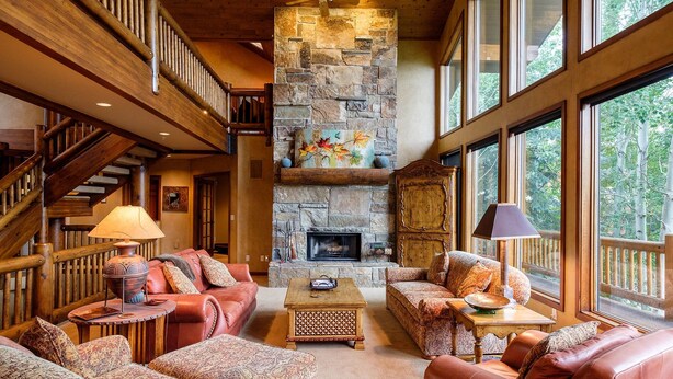 A spacious living room with a stone fireplace, leather sofas, and a wooden staircase. - 3390 Sun Ridge Dr (Park City)