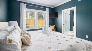 A bedroom with a bed, a window, a chair, and a door leading to a bathroom. - 21712 Palm Ave Stay Awhile (Panama City Beach)