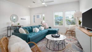 A modern living room with a teal sectional sofa, a round coffee table, and a TV on a wooden stand.