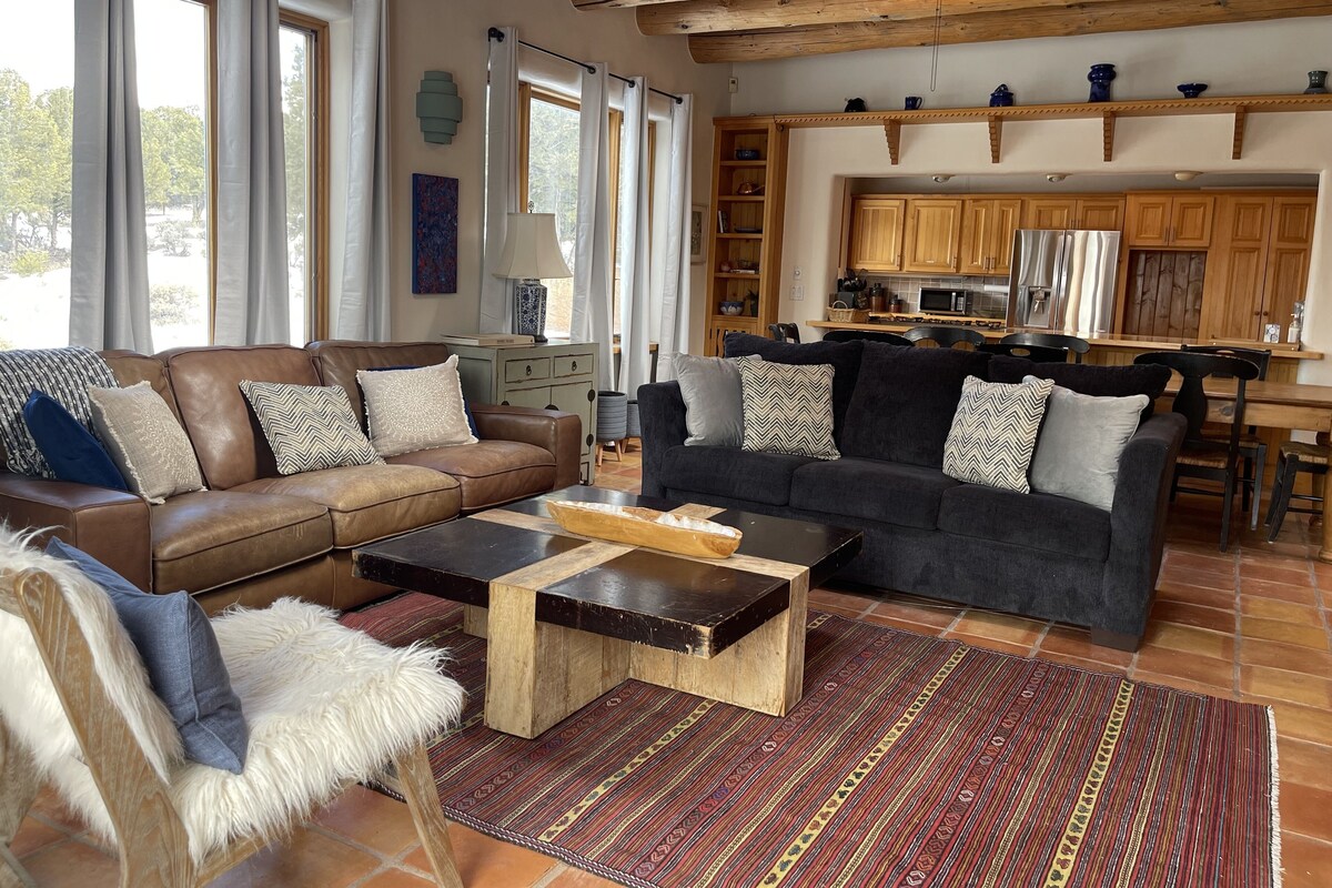 Een ruime zithoek met twee banken, een salontafel en een fauteuil met een bont plaid. Achtergrond toont een keuken met houten kastjes en een eethoek.