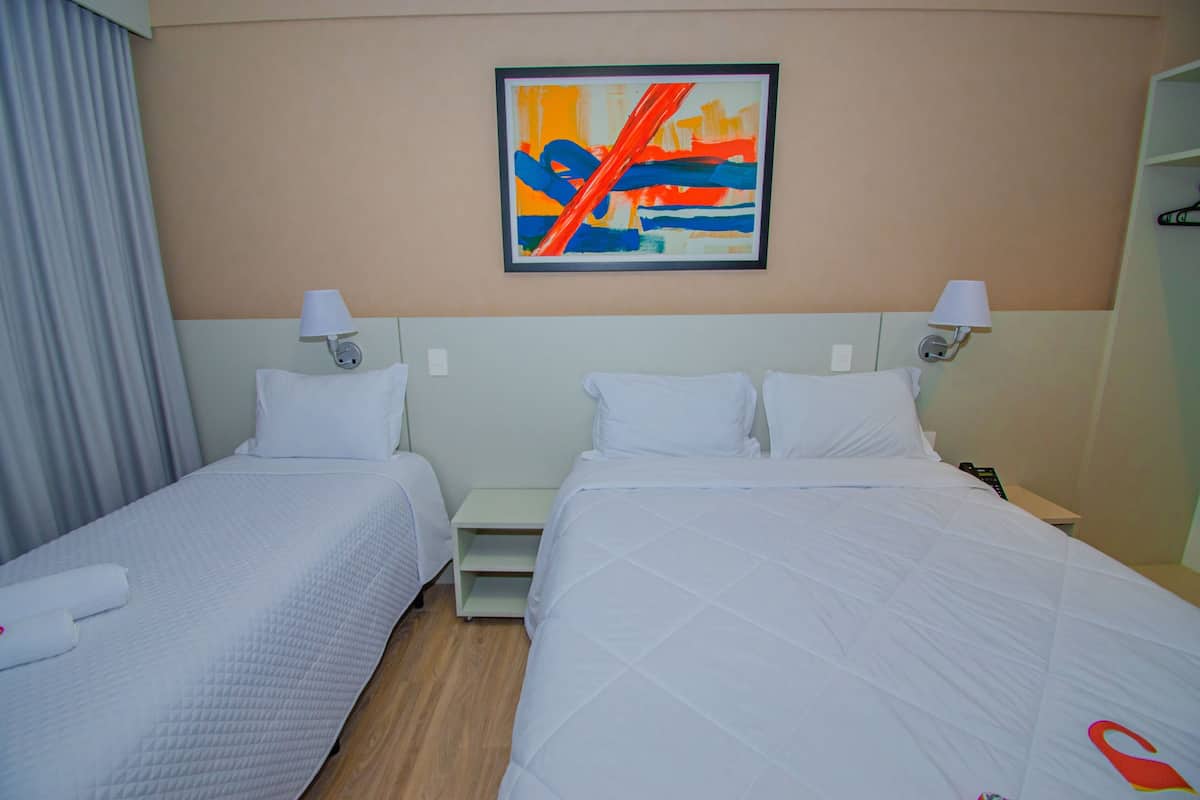 A hotel room with two beds, white linens, a nightstand, a wall-mounted abstract painting, and a window with curtains.