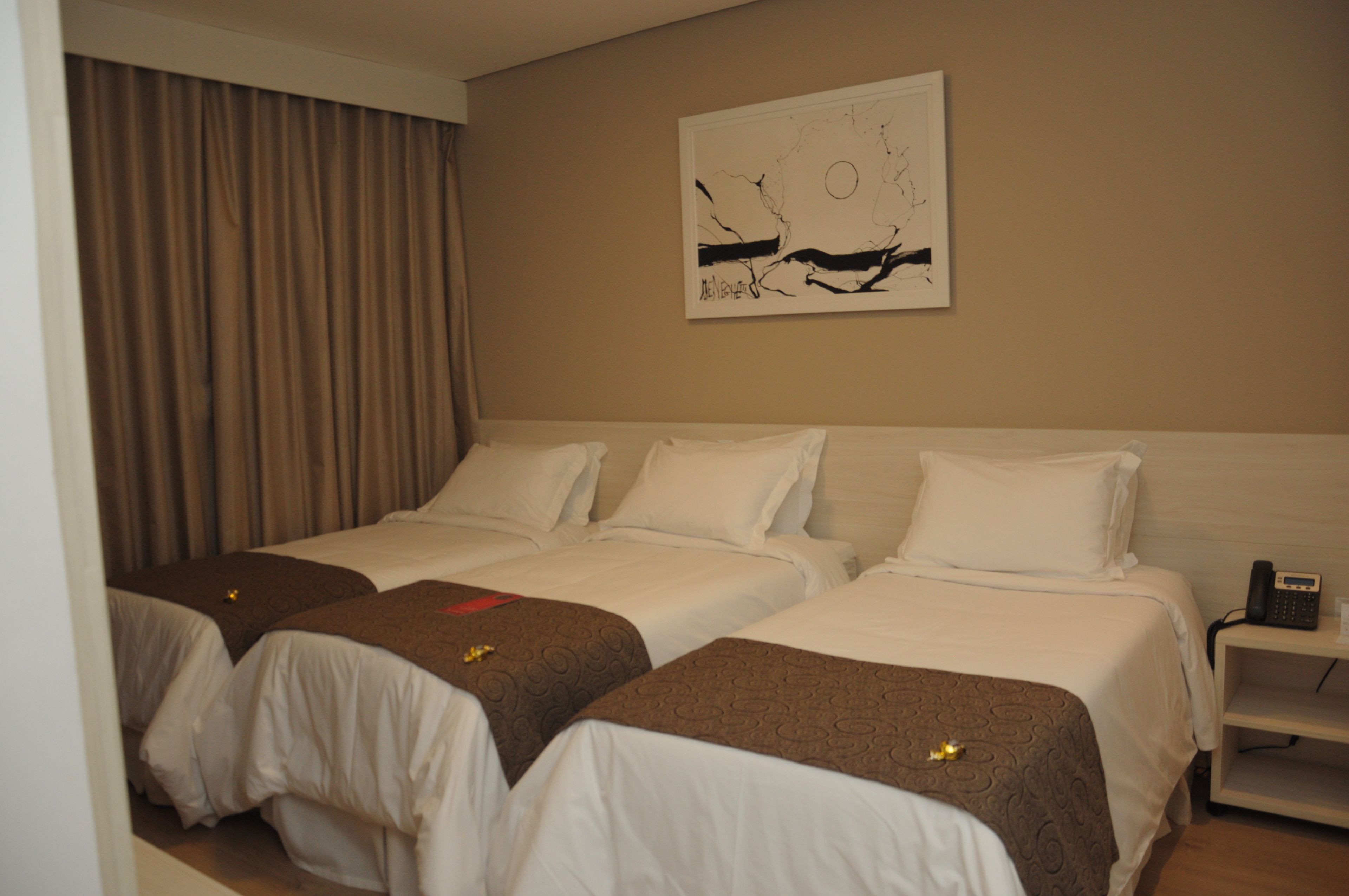 A hotel room with two beds, a large painting on the wall, a telephone on a bedside table, and a curtain covering a window.
