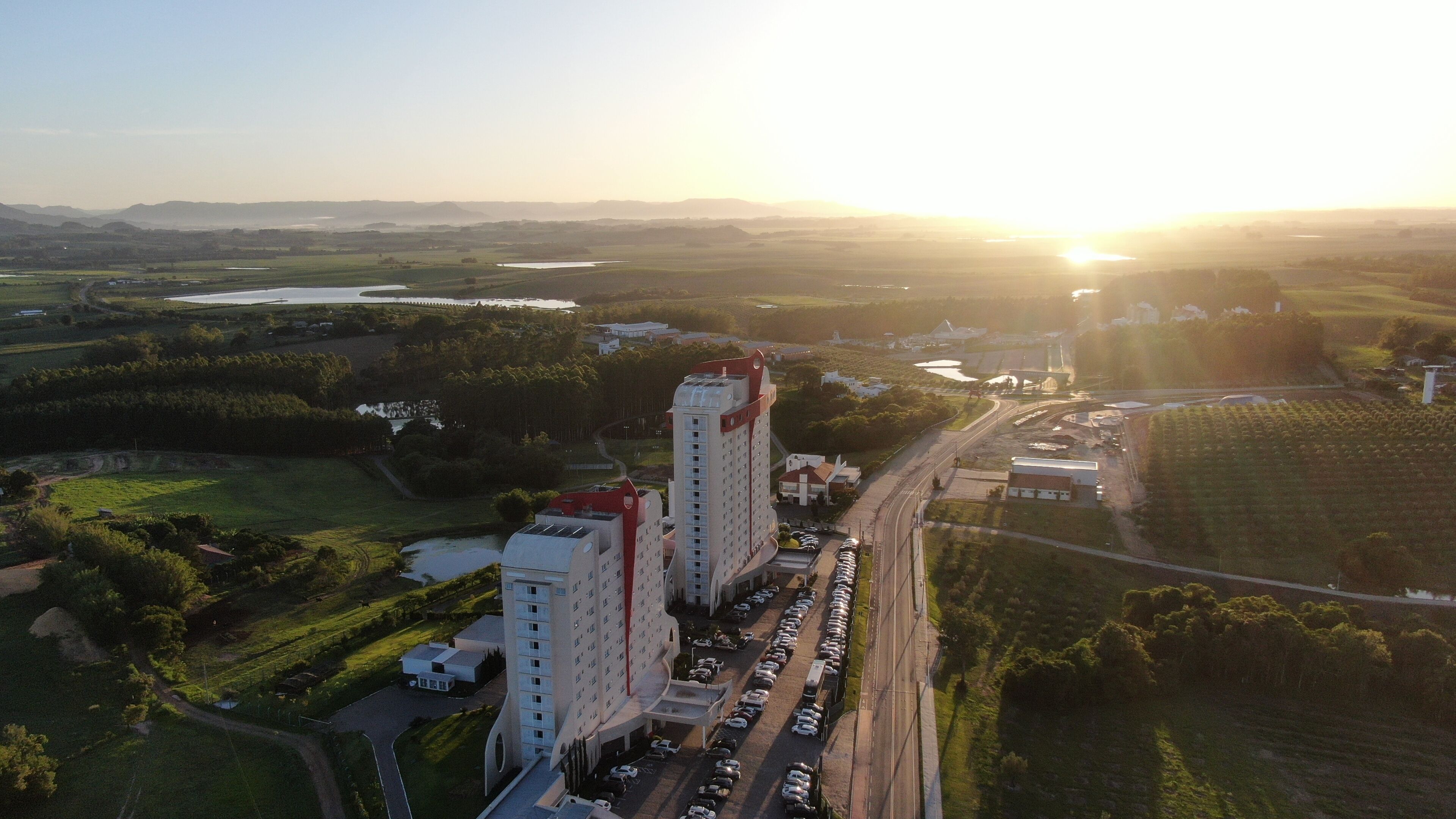 An aerial view of a hotel complex with multiple buildings, a parking lot, and surrounding greenery.