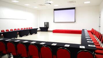 A conference room with a long table, red chairs, a projector screen, and a whiteboard.