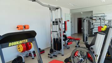 Un gimnasio con equipamiento de levantamiento de pesas, incluyendo una prensa de banca, una estructura para sentadillas y diferentes pesas.