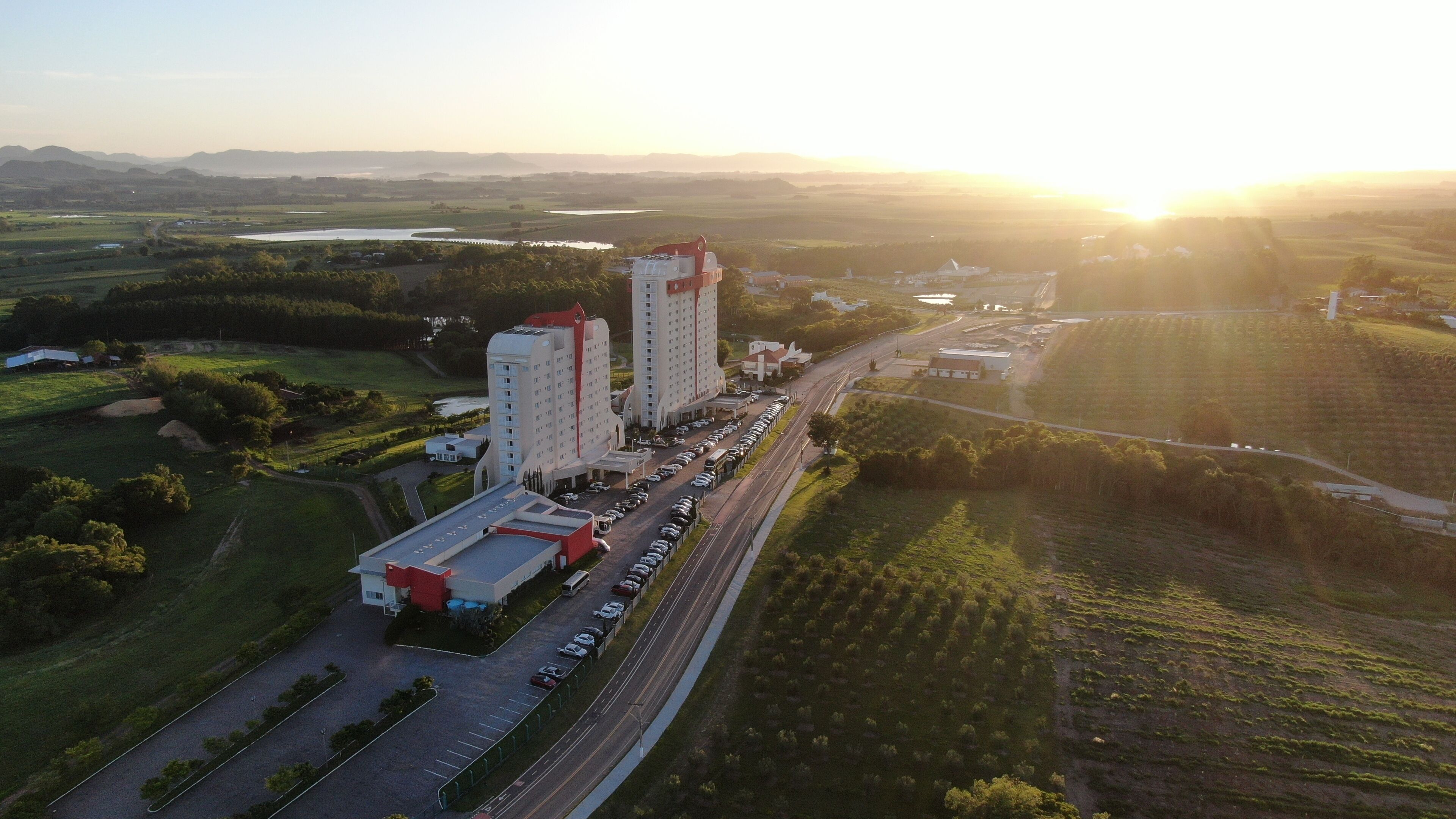 An aerial view of a hotel complex with multiple buildings, a parking lot, and surrounding fields.