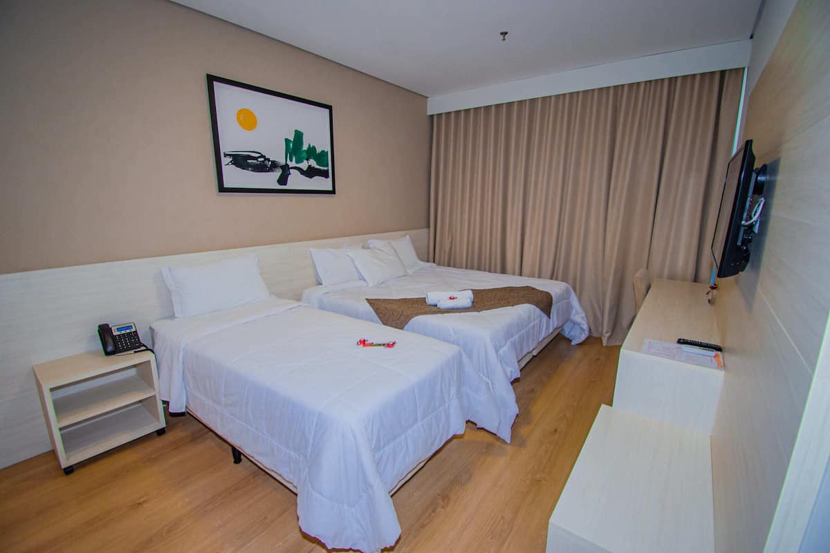 A hotel room with two beds, a bedside table with a phone, a TV, and a painting on the wall.
