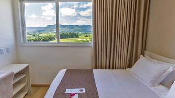 Habitación de hotel con una cama, un escritorio y una ventana con vistas a colinas verdes.