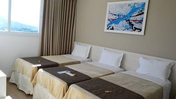 A hotel room with two single beds, a large window with curtains, and a painting on the wall.