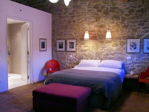A bedroom with a stone wall, a bed with white linens, a red chair, and a small table with a lamp. - the Pigsties - 3 people Casale Monticchio, a 17th century farmhouse (Marsciano)