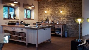 Una cocina con una isla central, paredes de piedra, lámparas colgantes y un techo de madera rústica.
