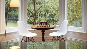 A chessboard on a round table with two white chairs, set in front of a large window with a view of greenery. - A substantial six double bedroom property located in the heart of St Agnes. (St Agnes)