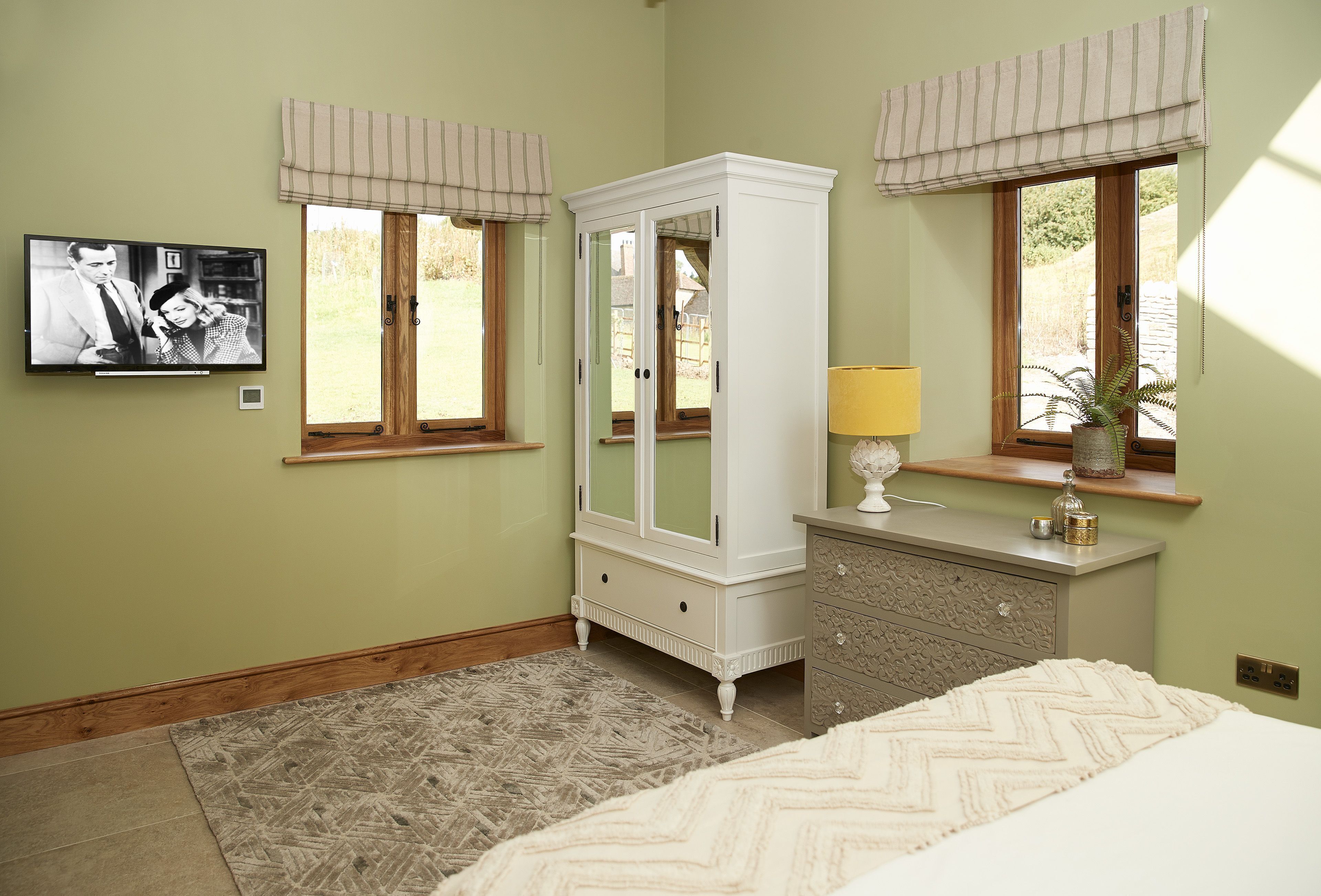 Een slaapkamer met een bed, een dressoir, een spiegel en een televisie aan de muur.
