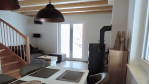 A modern living room with a wooden staircase, a fireplace, and a dining area with a table and chairs.