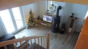 A cozy living room with a wooden staircase, a Christmas tree, a fireplace, and a television.