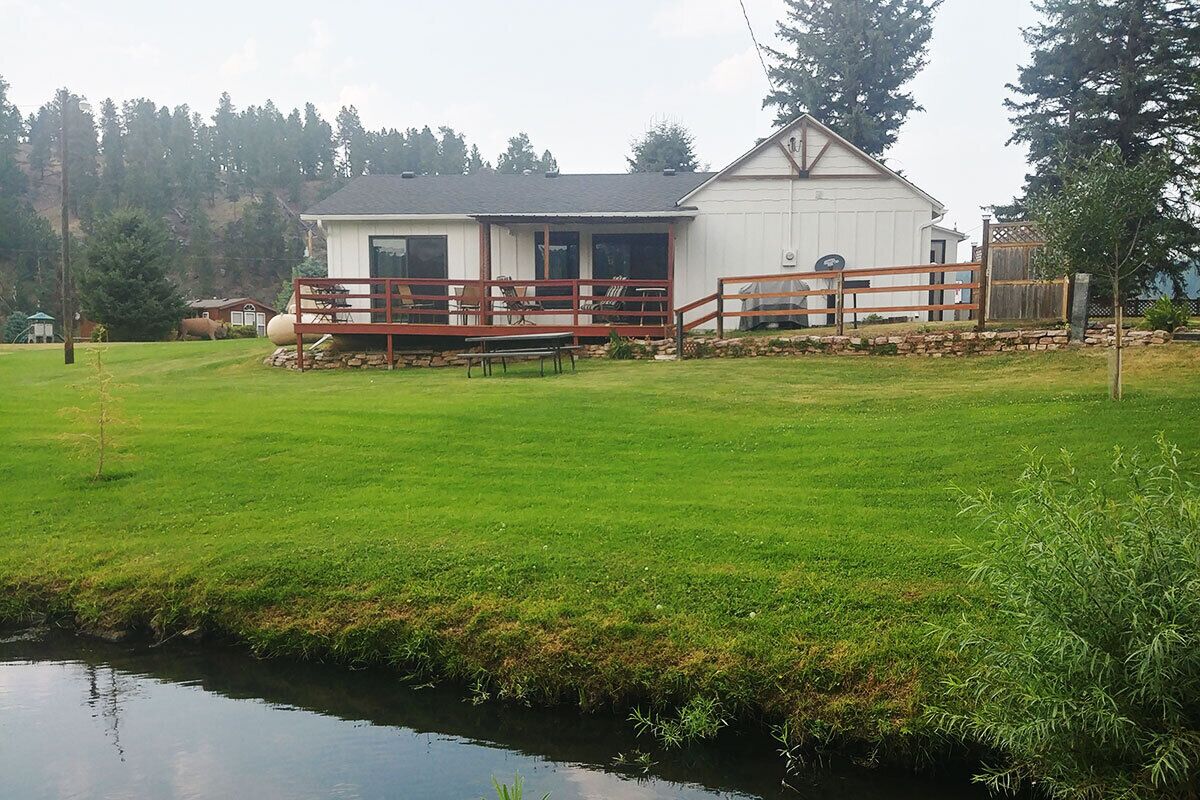 A two-story house with a covered porch and a small pond in front.