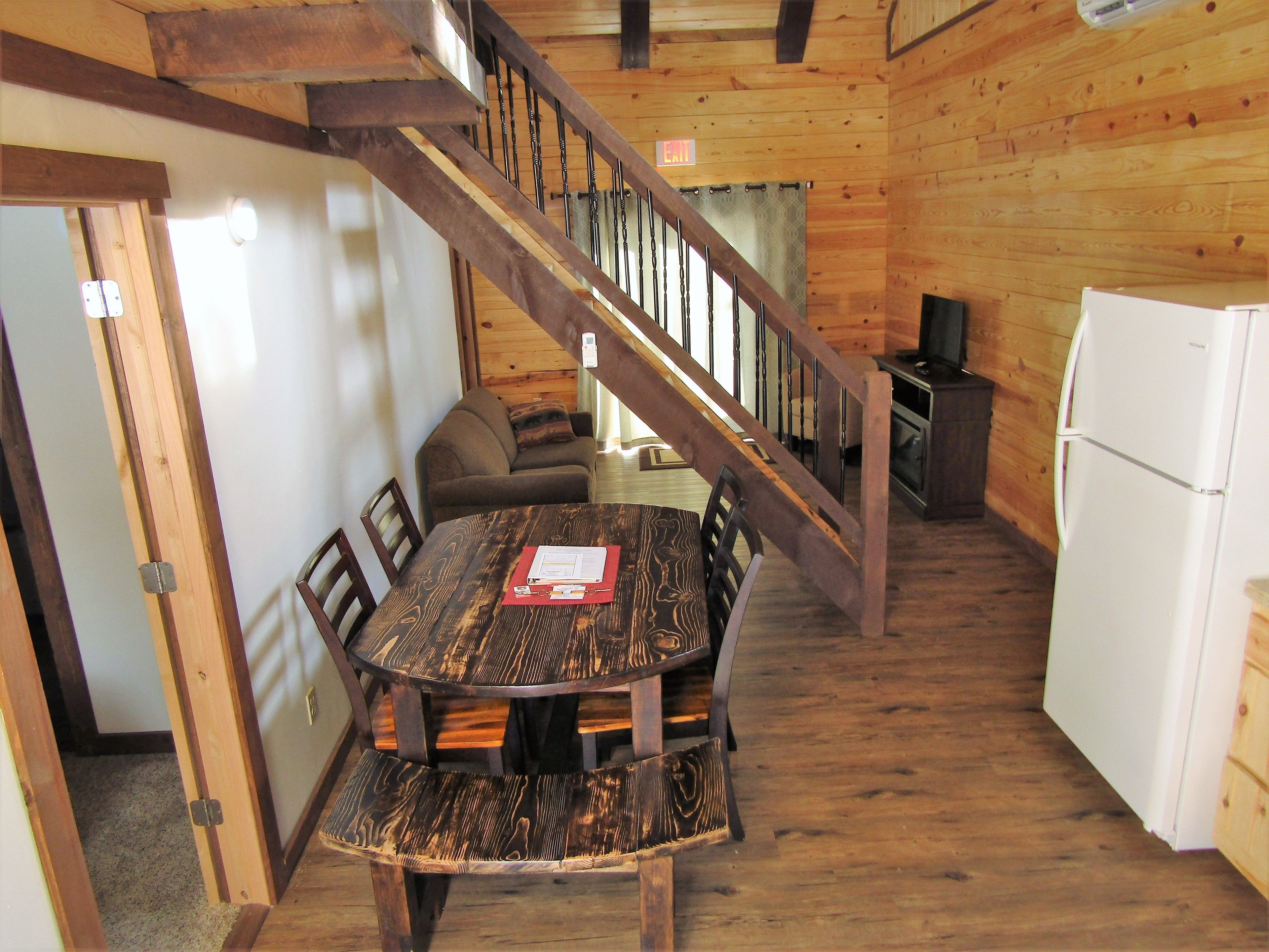 A wooden interior with a dining table, chairs, a staircase, and a refrigerator.