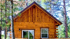 A wooden cabin with a porch, large windows, and a grill outside. - Freedom Ridge Cabins (Hill City)