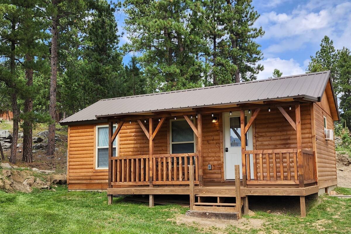 A small wooden cabin with a porch, surrounded by trees.