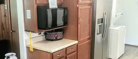 A kitchen with wooden cabinets, a microwave, a refrigerator, and a small sink.