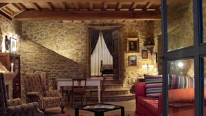 Una habitación rústica con paredes de piedra y techo de madera, amueblada con un sofá rojo, sillones estampados y una mesa de centro.