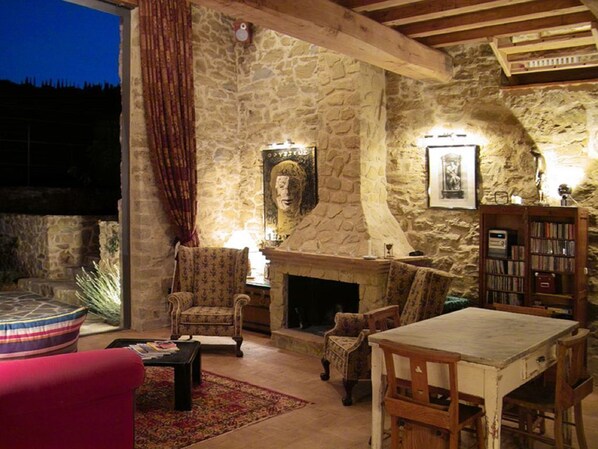 A stone-walled room with a fireplace, a sofa, a table, and a bookshelf. - The Barns - 5 people Casale Monticchio, a 17th century farmhouse (Marsciano)