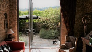 Habitación con paredes de piedra, un sofá rojo, un sillón estampado y vistas a un jardín a través de un ventanal.