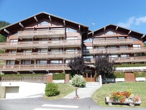 Un hôtel à plusieurs étages doté de balcons, d’une entrée principale et d’un jardin agrémenté de fleurs.