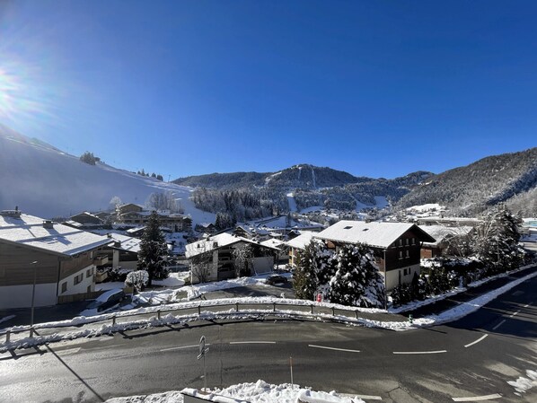 A snow-covered village with buildings, a parking lot, and a mountain backdrop.