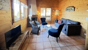 Ein gemütliches Blockhaushaus-Interieur mit Kamin, Korbstühlen, einer Couch und einem Fernseher.