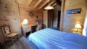Ein Zimmer in einer Holzhütte mit Bett, Schreibtisch, Stuhl und zwei Lampen.