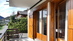 A wooden balcony with a metal railing, large sliding glass doors, and a view of a mountain landscape. - ABRICOT - Apartment in a chalet with a terrace and mountain views - Garage (La Clusaz)