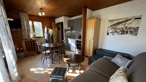 A cozy living room with a sofa, ottoman, and a dining table with chairs. There is a kitchen area with cabinets and a microwave. - ABRICOT - Apartment in a chalet with a terrace and mountain views - Garage (La Clusaz)
