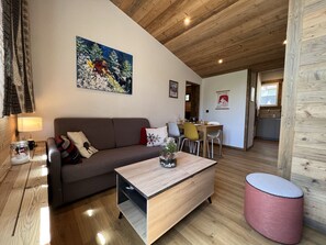 A cozy living room with a wooden ceiling, a sofa, a coffee table, and a dining area with chairs. - OURS BLANC 29 - Duplex with mountain views, near the aquatic center - Wi-Fi - Garage (La Clusaz)